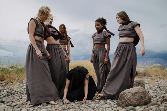 A group of diverse women standing and kneeling on a rocky field, conveying unity.