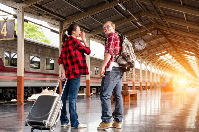 Young couple in a railway station, ready for travel. Bright morning scene with backpacks and luggage.