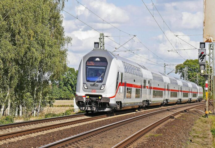 A sleek double-decker train traveling on rural railway tracks on a sunny day.